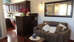 Ein Wohnzimmer mit einer Couch, einem Couchtisch, einer Vase mit Blumen und einer Küchenzeile im Hintergrund.