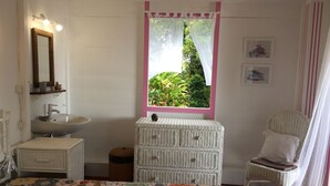 Ein Schlafzimmer mit Bett, Fenster mit Blick auf Grünflächen, Nachttisch, Stuhl und Spiegel.