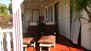 Eine überdachte Veranda mit zwei Holzstühlen und einer Bank, weißen Wänden und einem roten Boden.