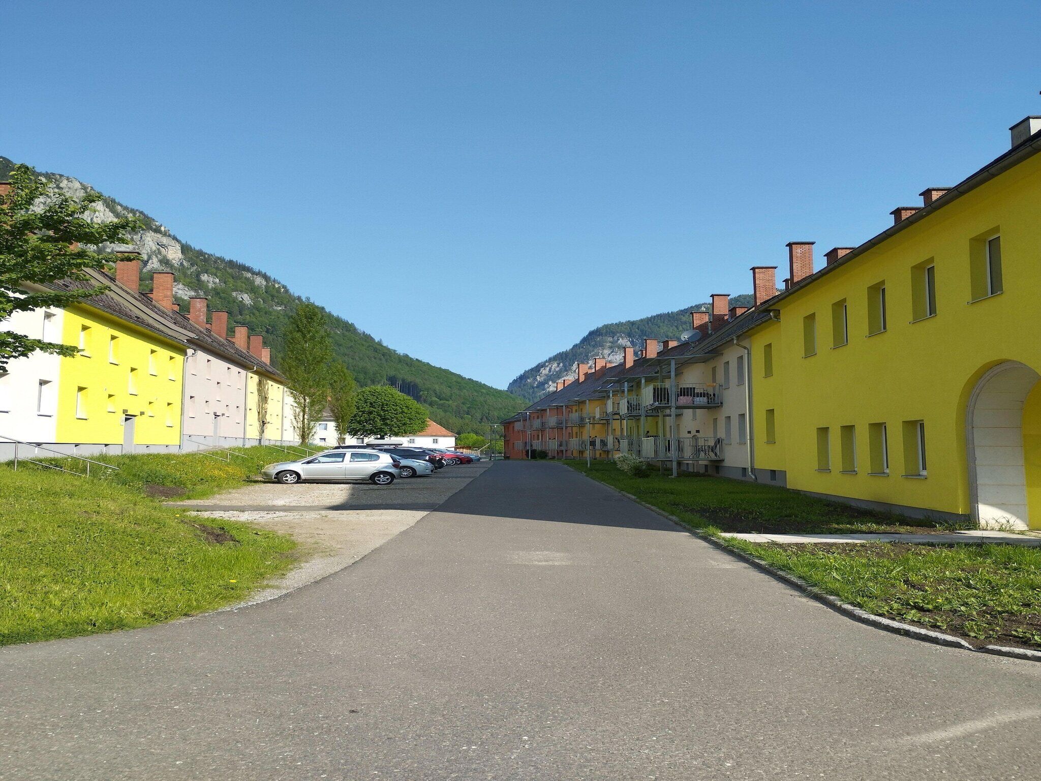 Une rue bordée de bâtiments aux couleurs vives, un ciel dégagé et une chaîne de montagnes en arrière-plan.