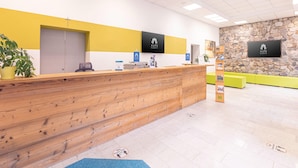A reception area with a wooden reception desk, a stone wall, and a mounted TV screen displaying the hotel's logo. - Lush apartment in Styria with infrared sauna (No Deposit) (Eisenerz)