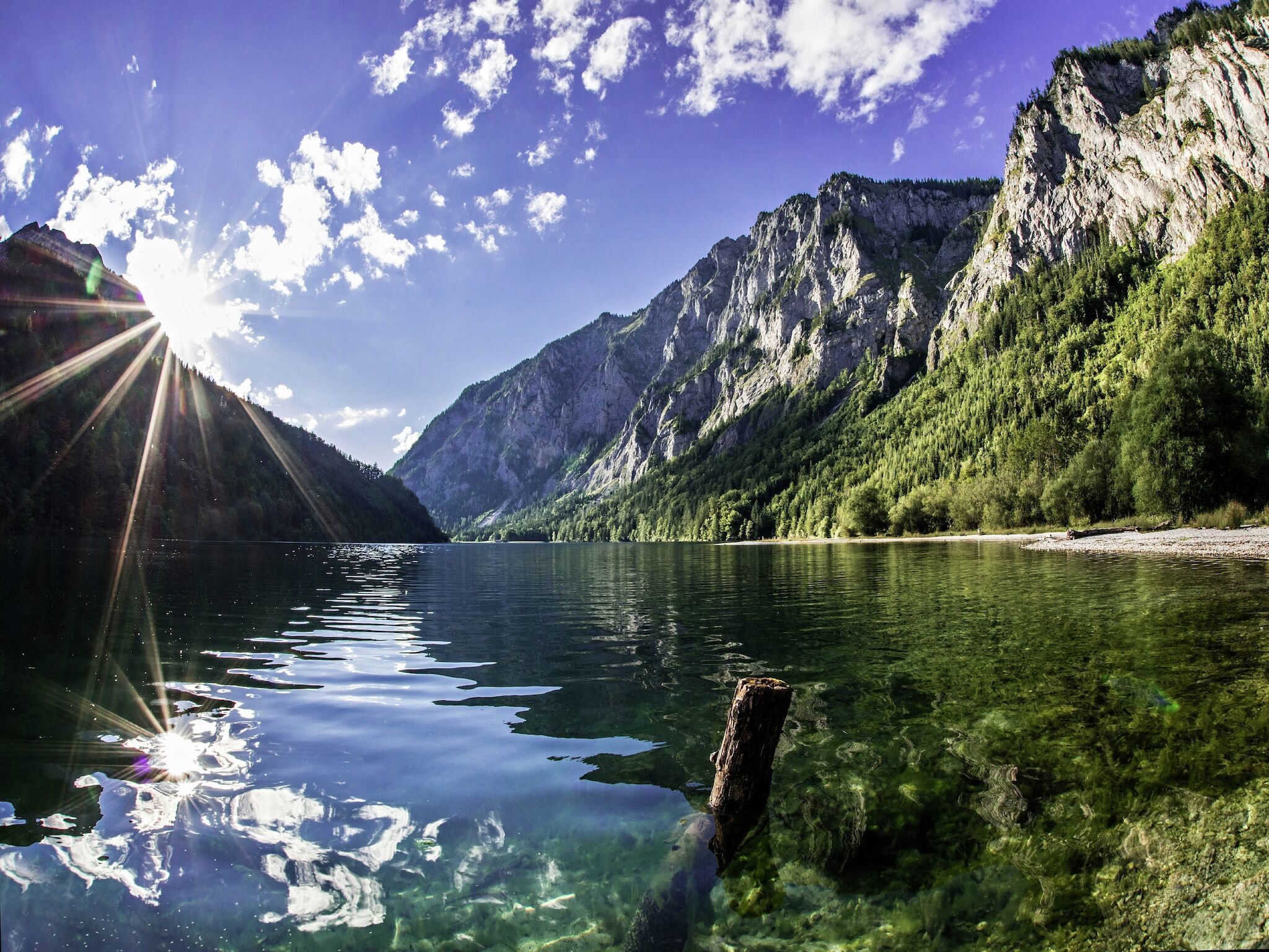 A clear lake with a rocky mountain backdrop and a wooden post in the water.