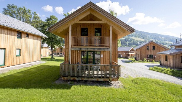 A wooden chalet with a balcony, surrounded by other similar buildings, set in a grassy area with mountains in the background. - Attractive chalet on the slopes (Kreischberg Murau)