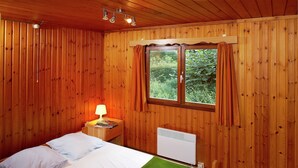 Una habitación con paneles de madera, una cama, una mesita de noche con lámpara y un ventanal con cortinas.