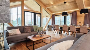 Un vaste espace de vie doté d’un plafond haut, de poutres en bois et de grandes fenêtres offrant une vue sur l’extérieur.