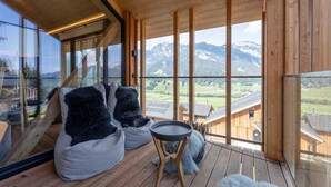 Un intérieur moderne avec un plafond en bois, de grandes fenêtres offrant une vue sur les montagnes et des coins salon confortables.