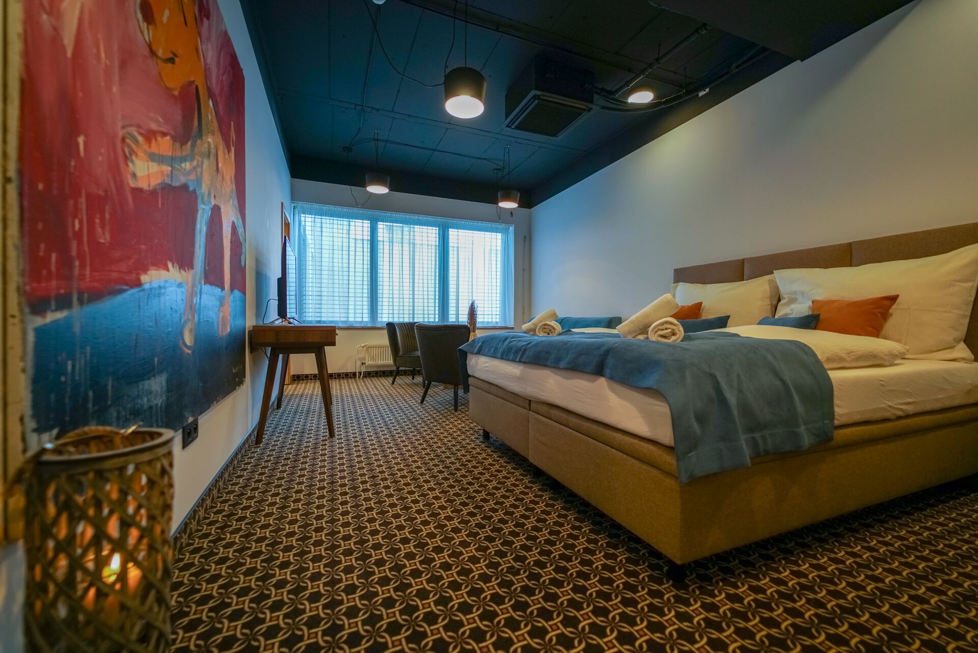 A bedroom with a patterned floor, a bed with multiple pillows, a desk, and a chair.