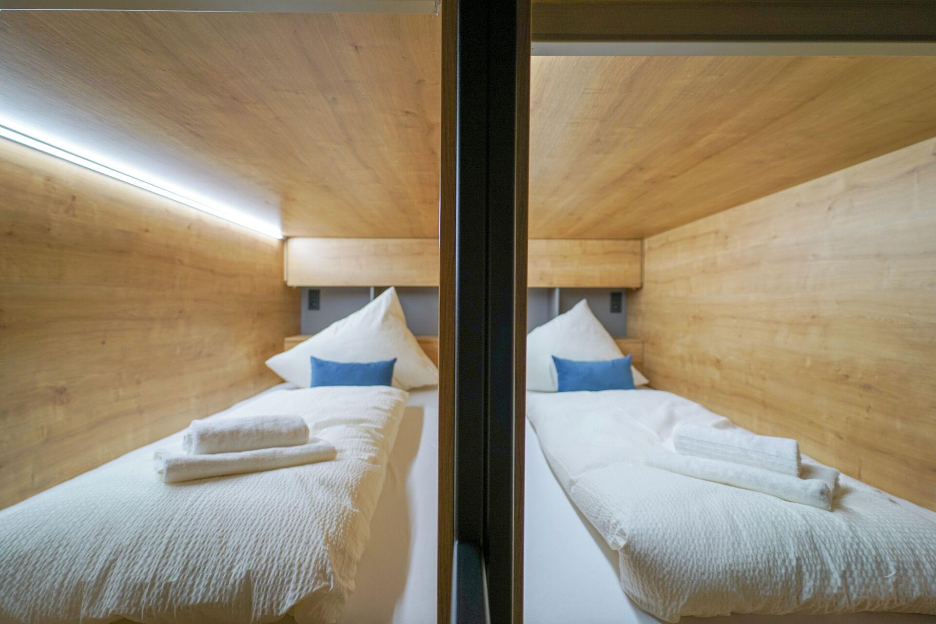 A mirrored room with wooden walls, two beds with white linens and blue pillows, and a visible light fixture.