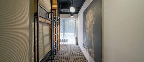 A hallway with patterned flooring, a large abstract painting on the wall, and a window with blinds.