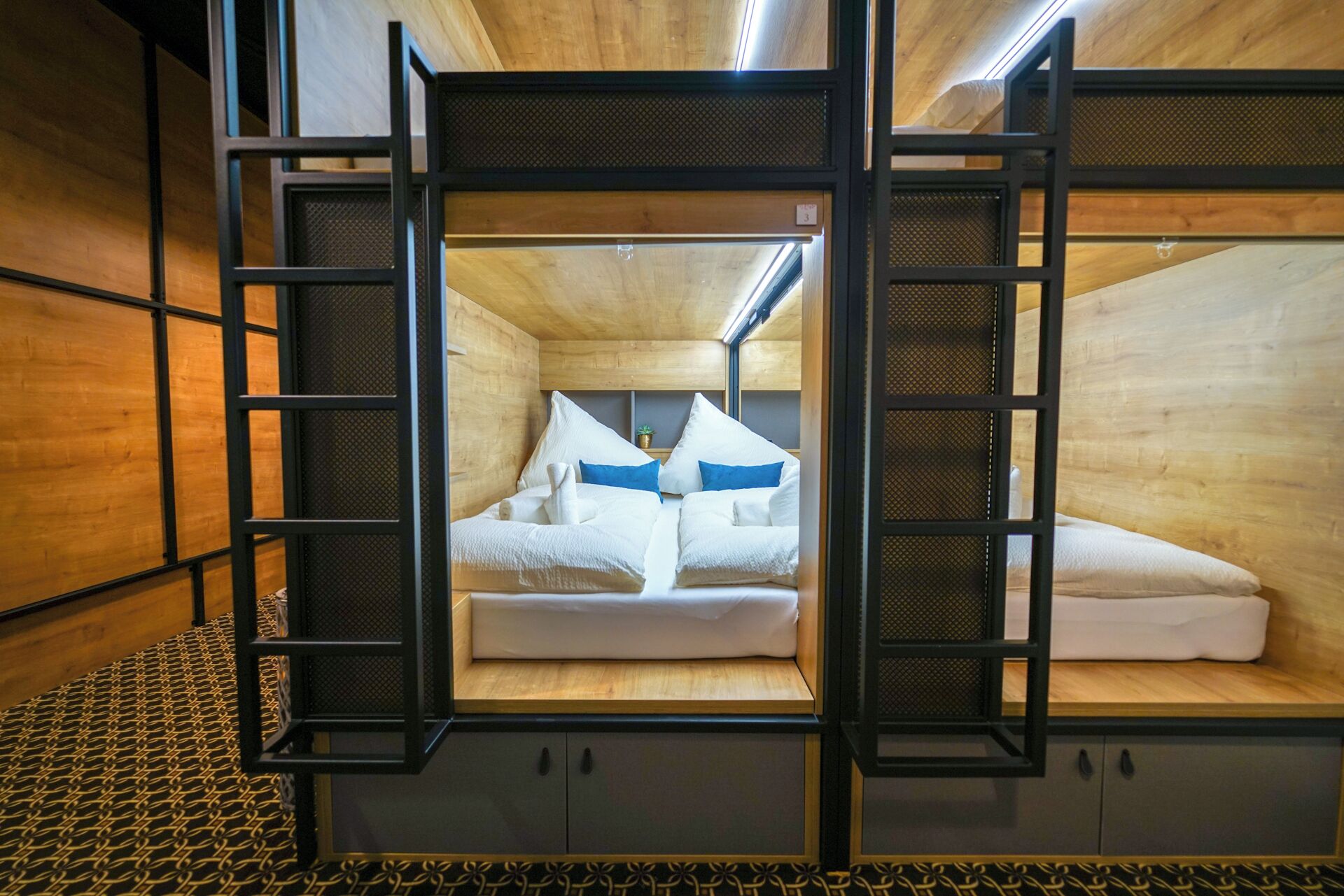 A compact, cabin-style room with a bunk bed, wooden walls, and a metal-framed window.