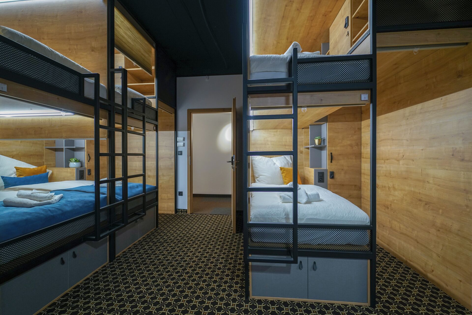 Habitación con literas, suelo estampado, paredes de madera y una pequeña planta en un estante.