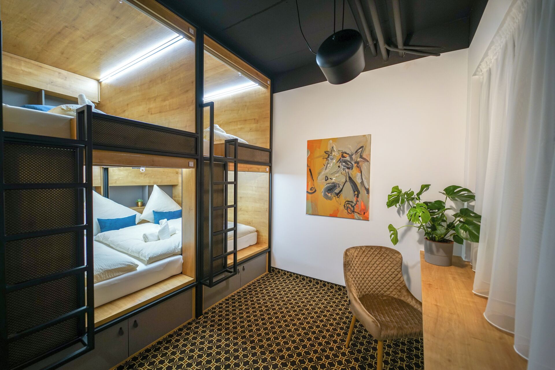 A compact room with a bunk bed, a desk, a chair, a potted plant, and a painting on the wall.