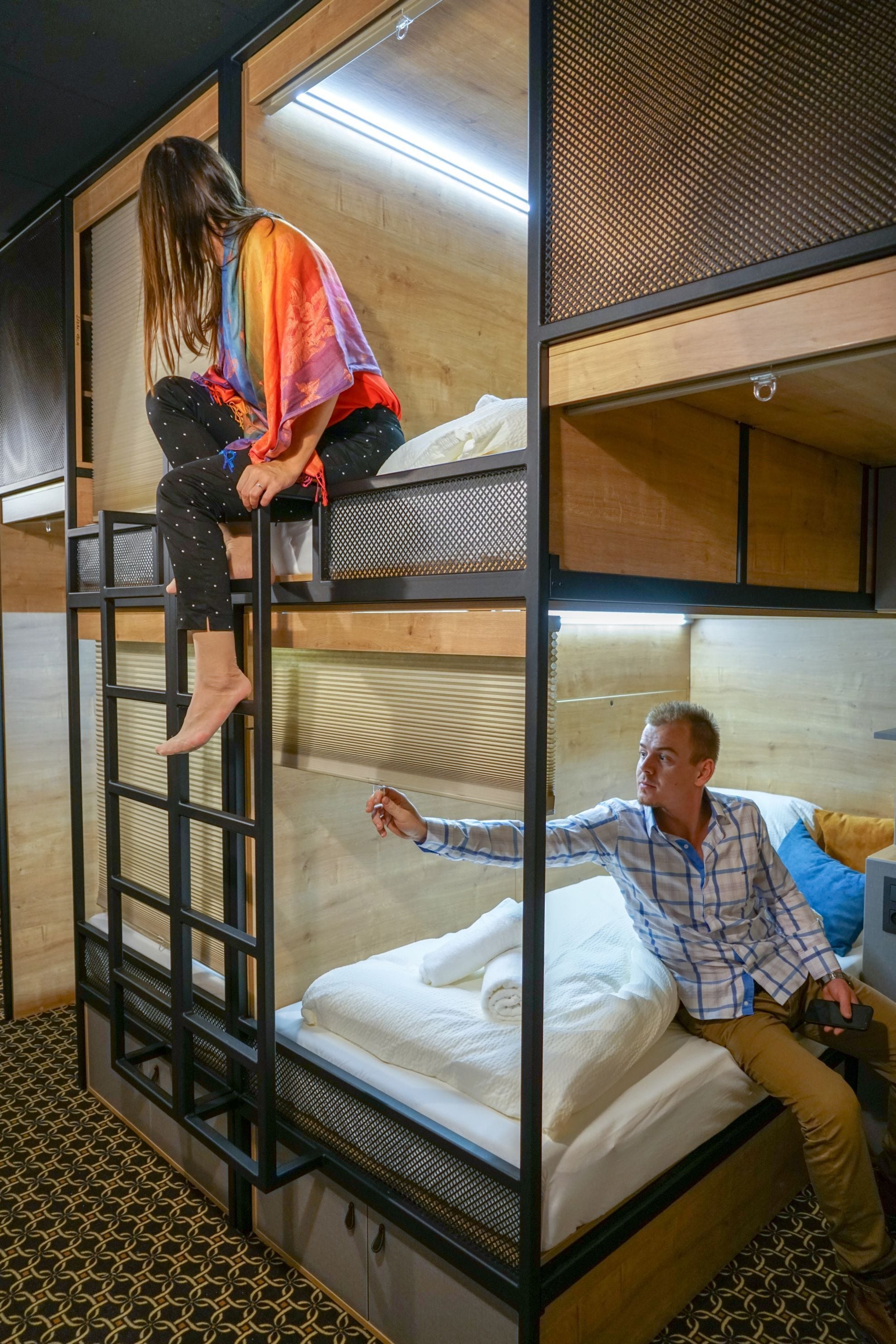 A bunk bed room with a ladder, a person climbing the ladder, and another person sitting on the lower bunk.