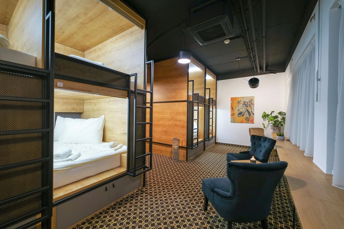 A modern hotel room with bunk beds, a patterned carpet, a black chair, and a painting on the wall.