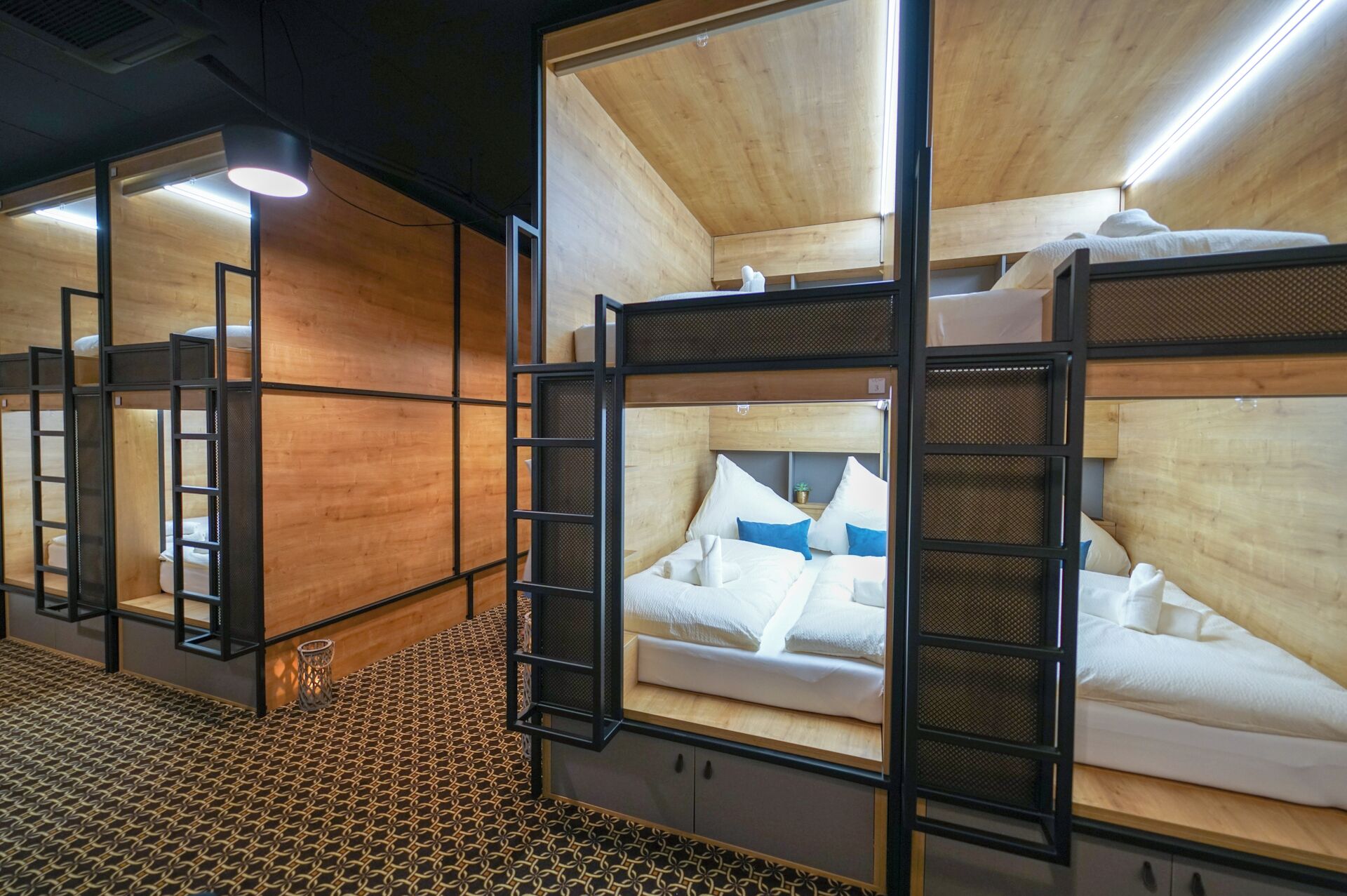 A series of bunk beds with wooden frames and metal mesh sides, arranged in a row with a patterned floor.
