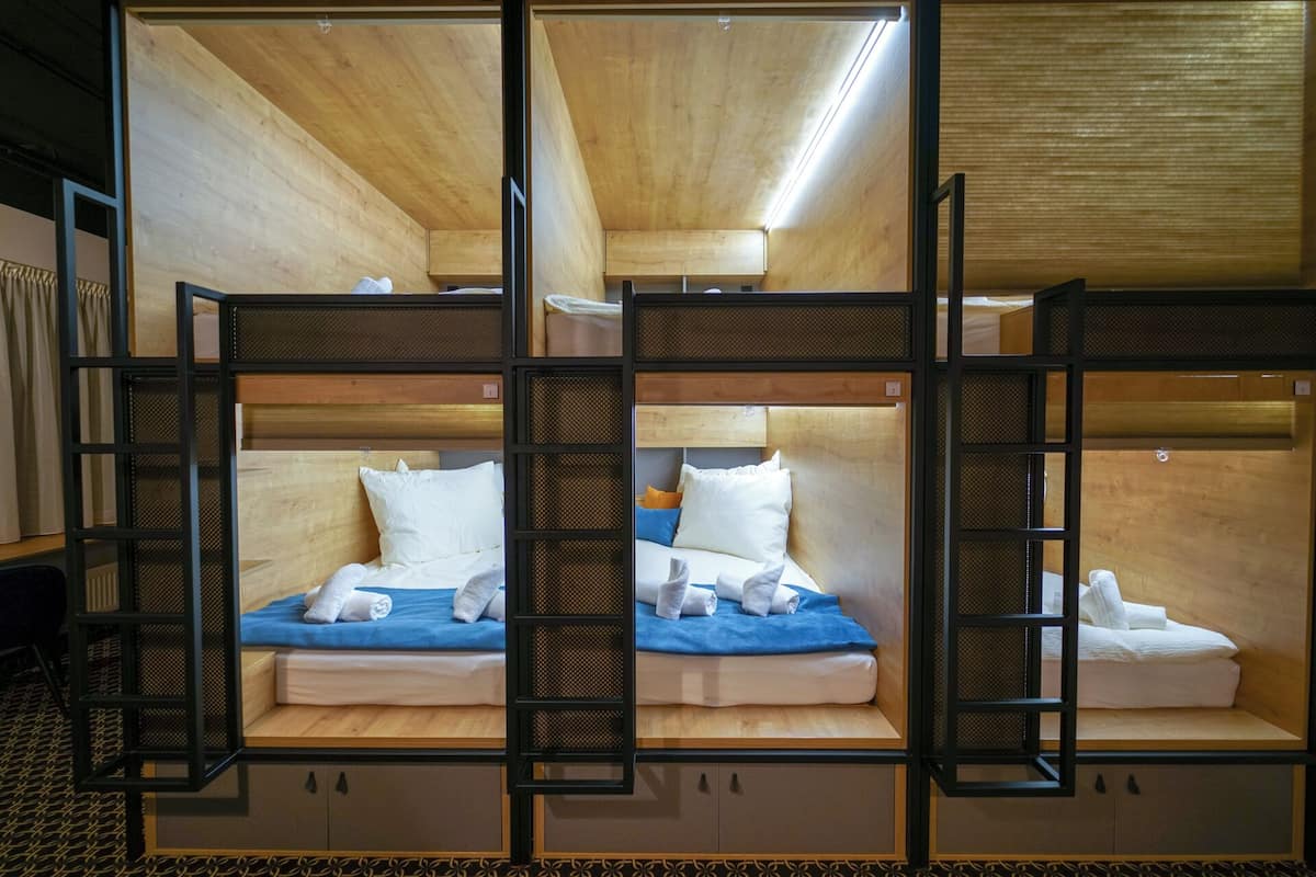 A room with bunk beds, each with a wooden headboard and a mattress. There are two beds visible, and each bed has a pillow and a rolled-up towel.