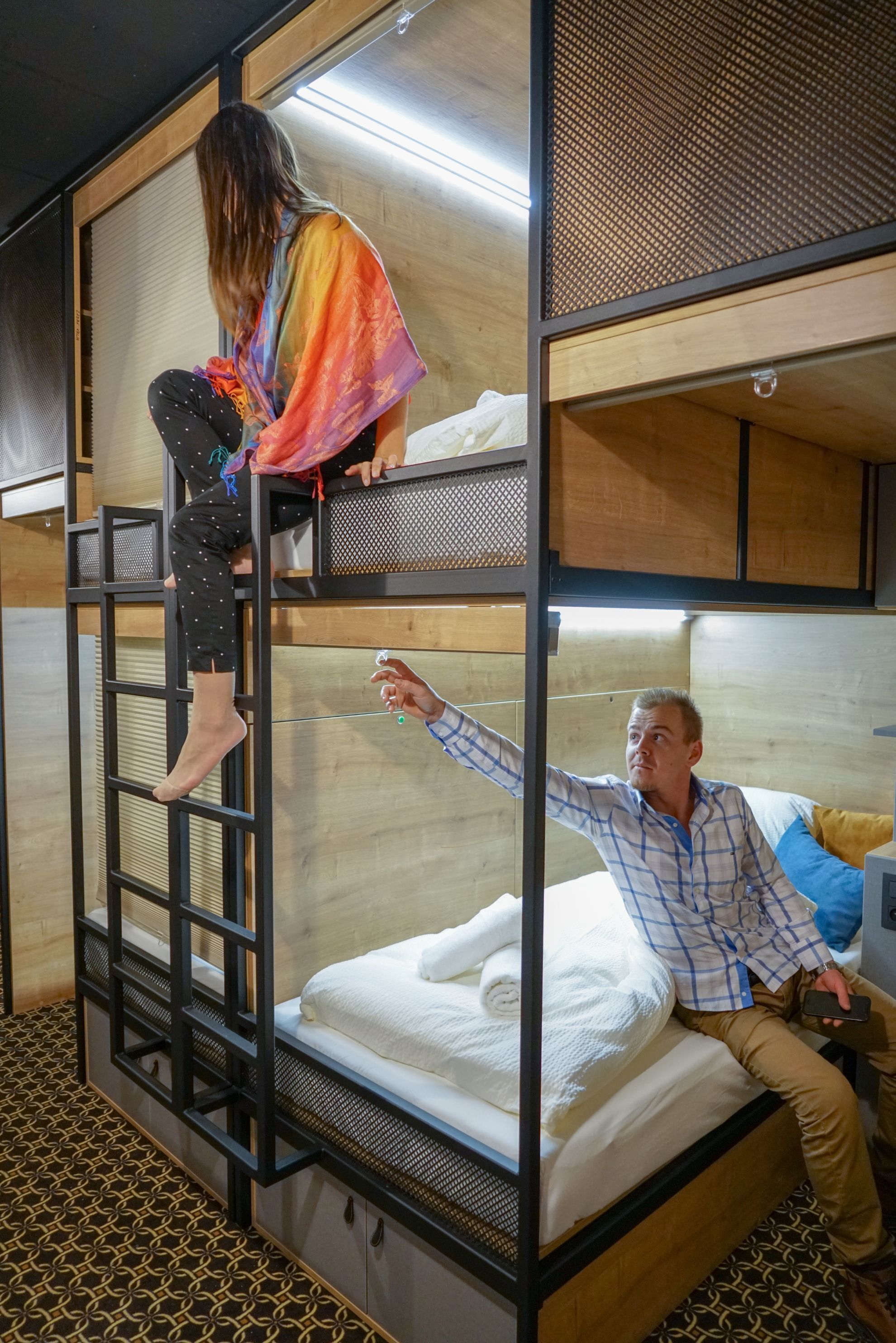 Una cama litera con una escalera, una persona escalando la escalera y otra sentada en la cama inferior.