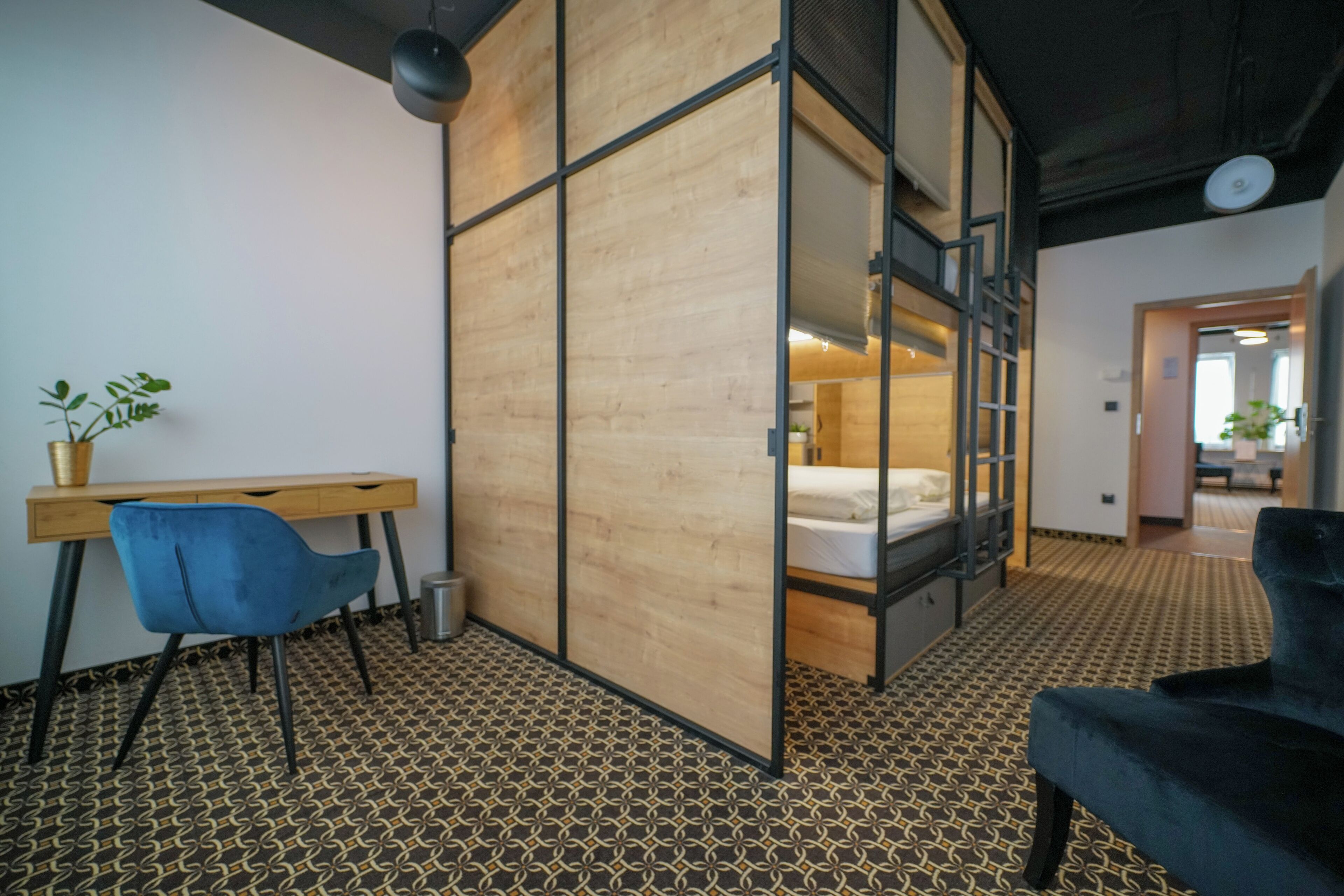 Una stanza con una scrivania in legno, una sedia blu, un letto a castello e un pavimento decorato.