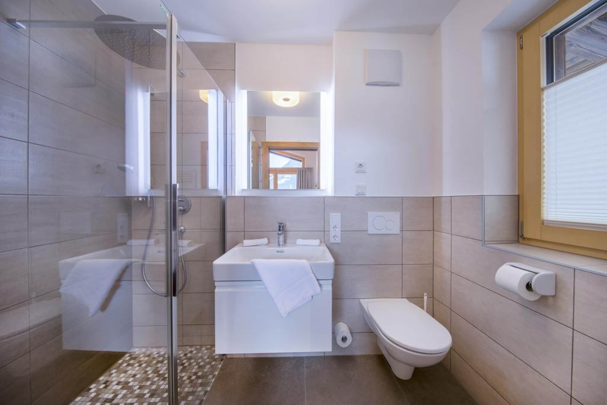 Een moderne badkamer met een douchecabine van glas, een wastafel met handdoek, een toilet en een raam met zonwering.