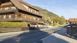 Un edificio tradicional de madera con un balcón, situado junto a una carretera con una montaña al fondo.