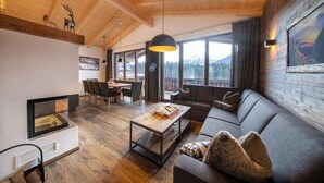 A cozy cabin interior with a fireplace, wooden ceiling, large windows, and a sofa. - Alpine Chalet with Sauna and Balcony (Neukirchen)