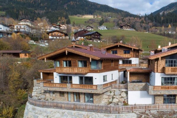 A mountain lodge with multiple wooden balconies, stone foundations, and a view of the surrounding mountainous landscape.