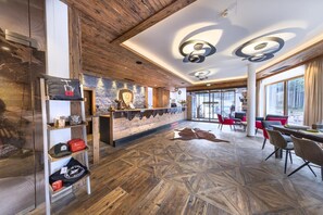 Un hall d’hôtel moderne avec un revêtement de sol en bois, un bar central et des espaces aménagés pour s’asseoir.