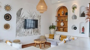 A modern living room with a large flat-screen TV, a wooden ceiling, and a variety of decorative items on the walls. - Good Vibe Villa - 3 Bdrm Luxury Villa (Canggu)