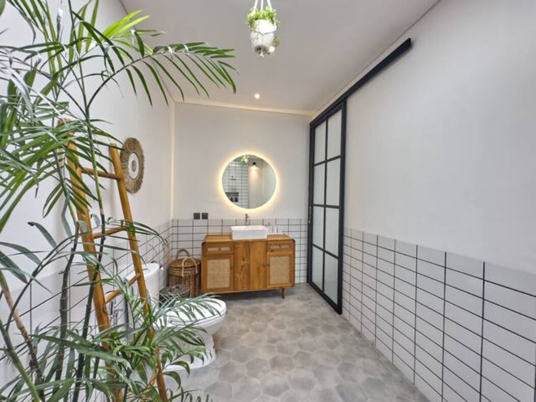 A modern bathroom with a wooden vanity, a round mirror, and a toilet.