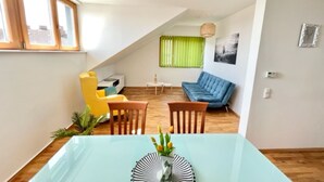 Uma sala de estar moderna com área de jantar, apresentando um sofá, cadeiras e uma mesa com um vaso de flores.