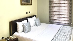 A hotel room with a bed, bedside table, and an air conditioning unit. - Nue Crest Hotel & Suites (Enugu)