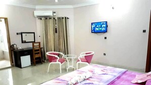 A hotel room with a bed, a desk, a chair, a TV, and an air conditioning unit. - Nue Crest Hotel & Suites (Enugu)