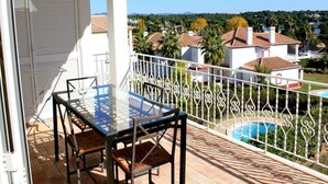 A balcony with a glass table and chairs, a pool, and a view of houses and greenery. - Presley Beije Apartment, Quinta do Lago, Algarve (Algarve)