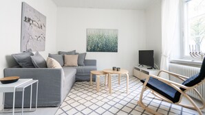A modern living room with a grey sofa, a rocking chair, a small table, and a TV. - Luminous 1br next to Puu-Vallilla (Helsinki)