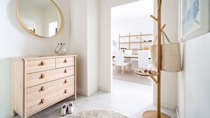 A minimalist room with a wooden dresser, a round mirror, and a coat rack with a bag. - Luminous 1br next to Puu-Vallilla (Helsinki)