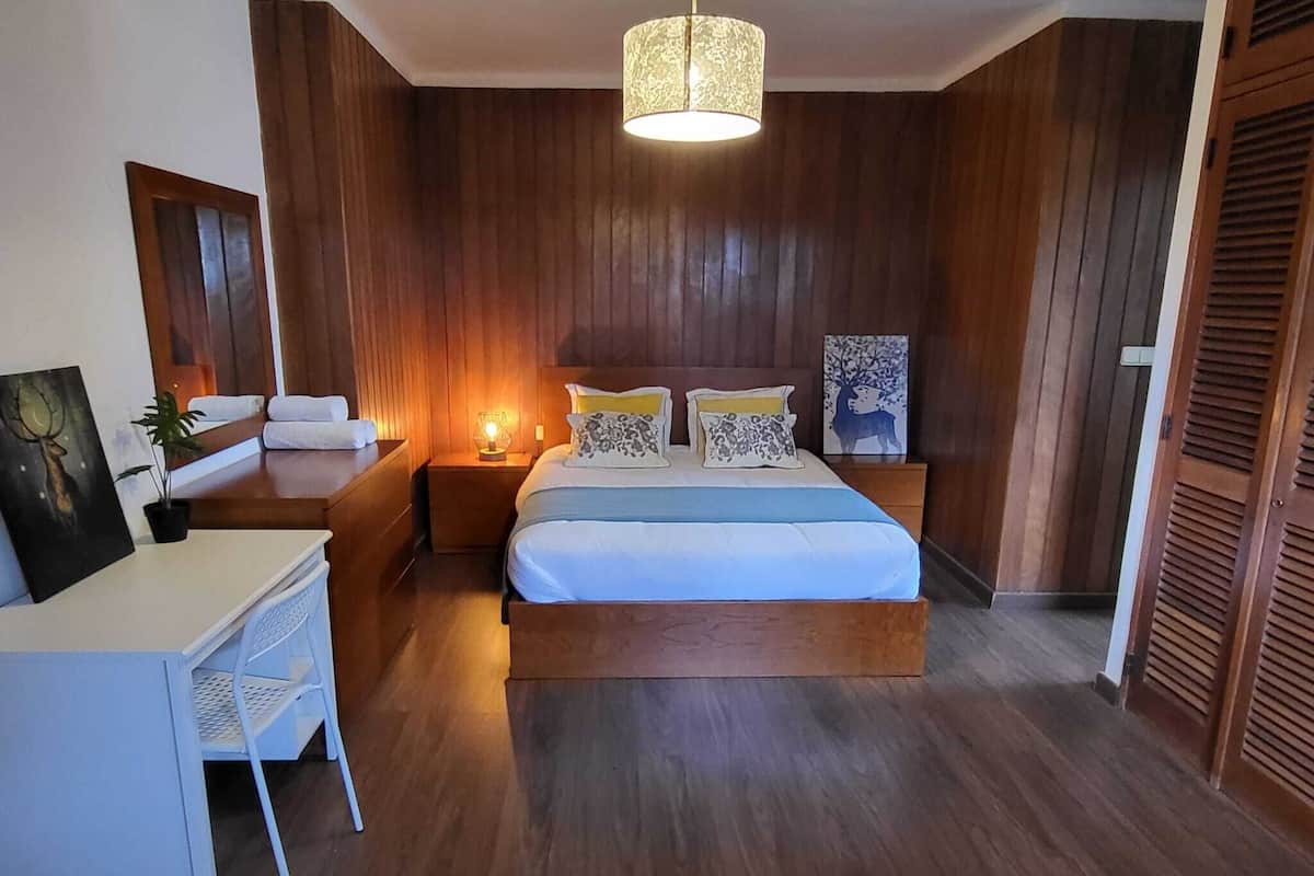 Ein Schlafzimmer mit einem Bett, Nachttischen, einem Schreibtisch und einer Pendelleuchte.