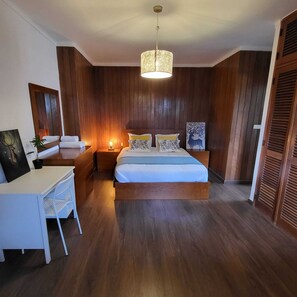 Un dormitorio con cama, mesitas de noche, un escritorio y una lámpara colgante.