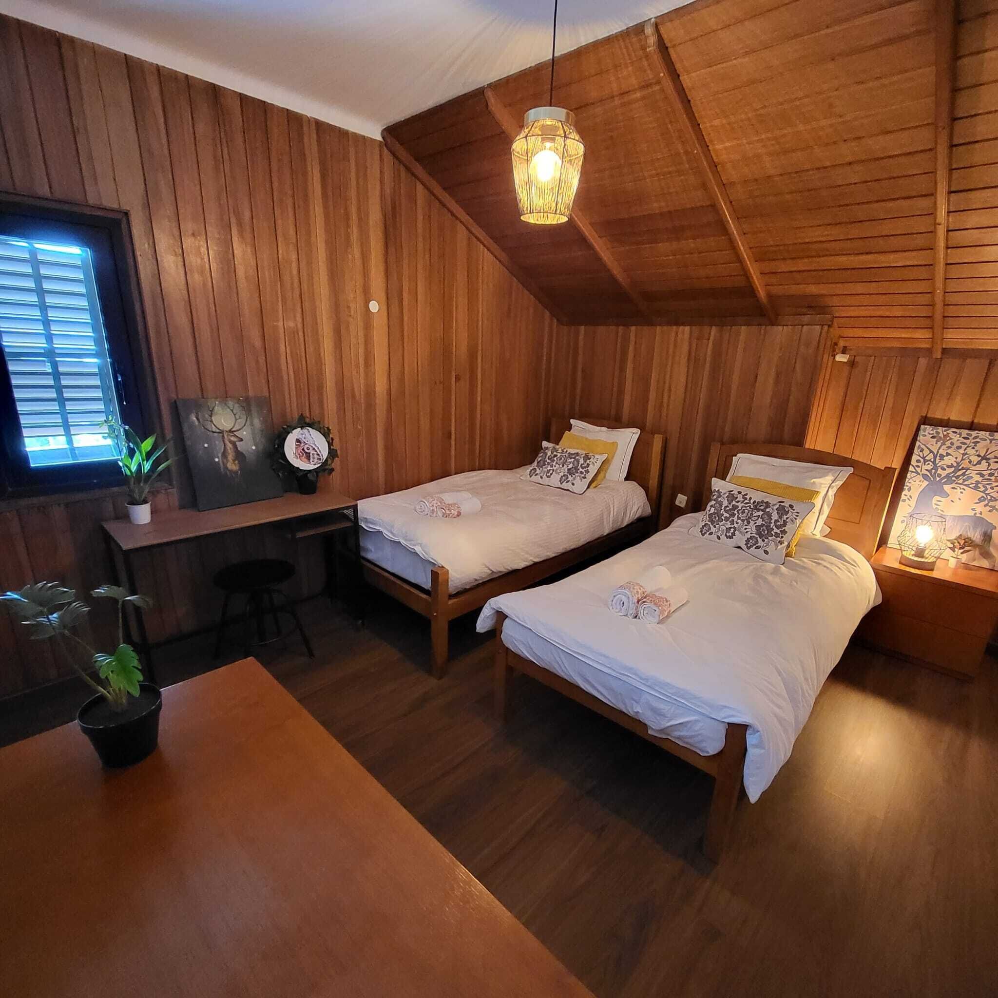 Une pièce chaleureuse avec deux lits en bois, un bureau et un luminaire suspendu.