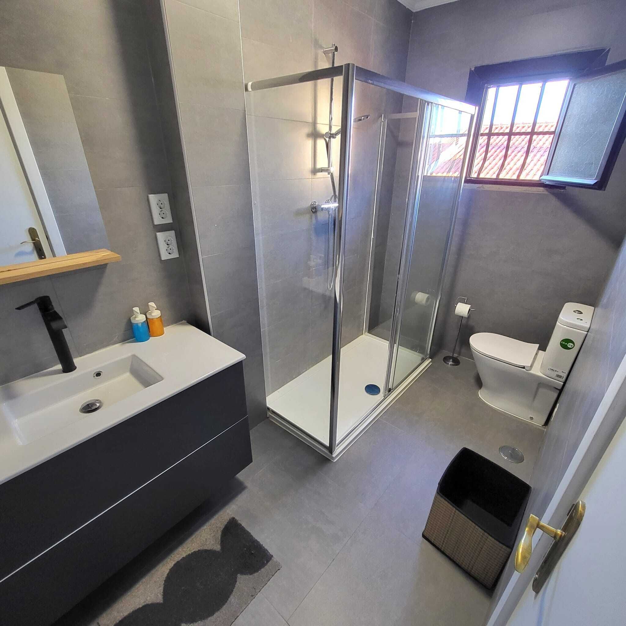 Une salle de bain moderne avec une douche à parois de verre, un lavabo blanc avec un robinet noir et des toilettes décorées d’un autocollant vert.