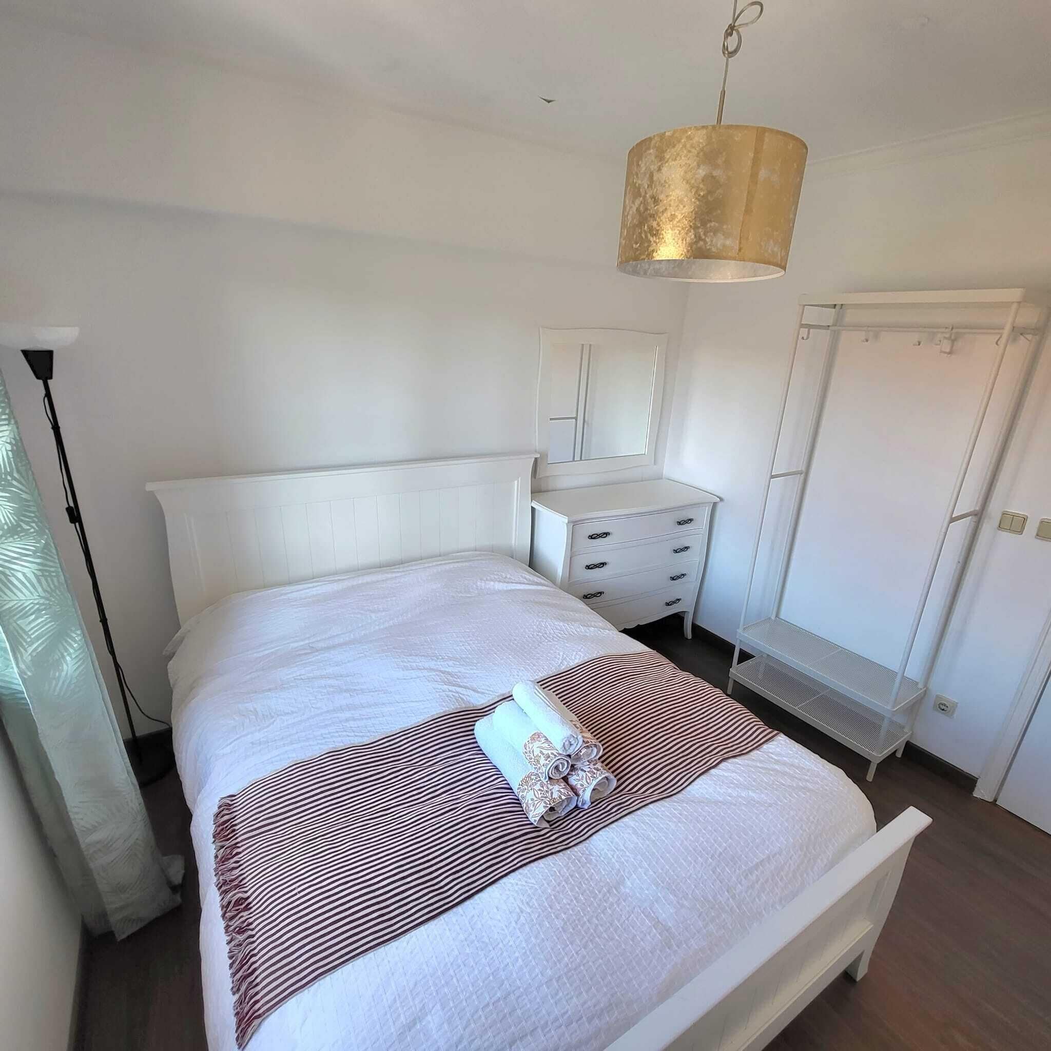 A neatly arranged bedroom with a bed, bedside table, dresser, and wardrobe.