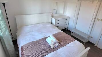 A neatly arranged bedroom with a bed, bedside table, dresser, and wardrobe.