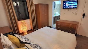 Un dormitorio con una cama grande, un armario, un televisor y un baño visible a través de una puerta abierta.