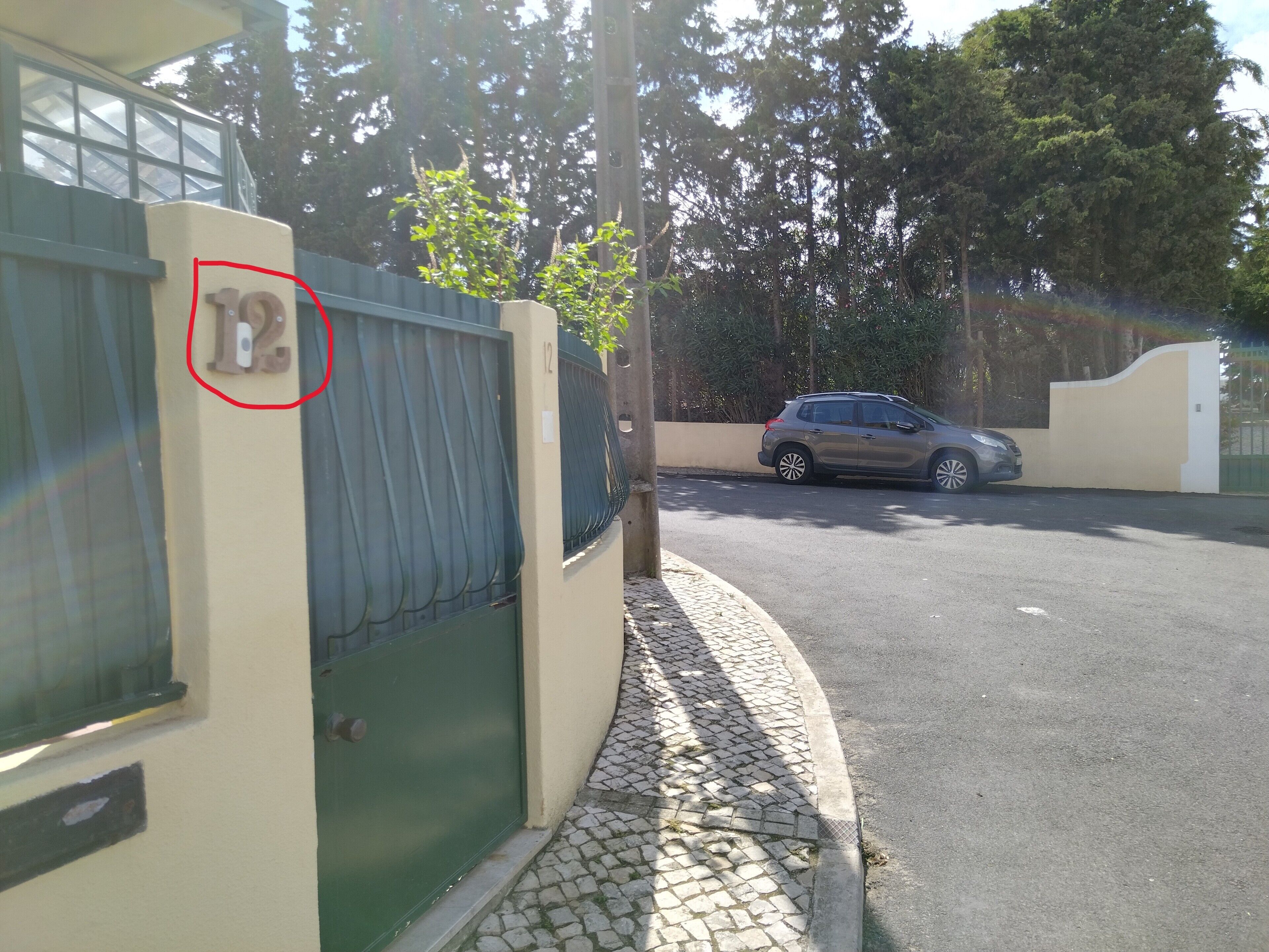 Une entrée fermée par un portail, avec une voiture garée à l’intérieur, un chemin pavé et un bâtiment portant un numéro.
