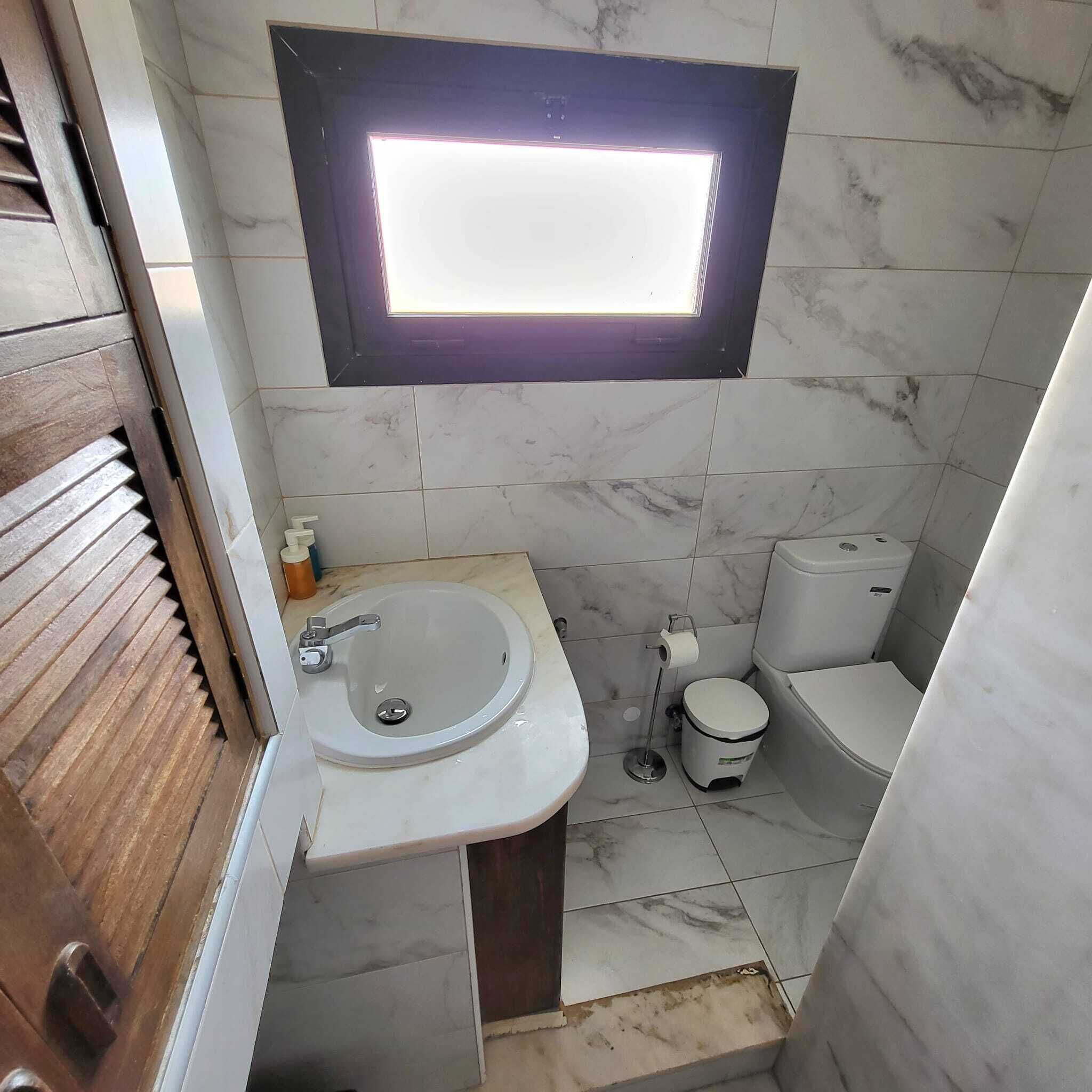 A bathroom with a sink, toilet, and a window above the sink.