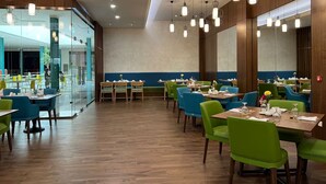 A spacious restaurant with wooden floors, green and blue chairs, and pendant lighting. - Ayla Ibri Hotel and Mall (Ibri)