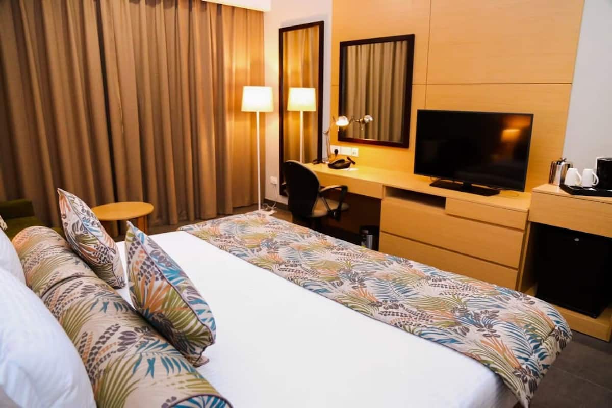 Una habitación de hotel con cama, escritorio con televisor, silla y cafetera.