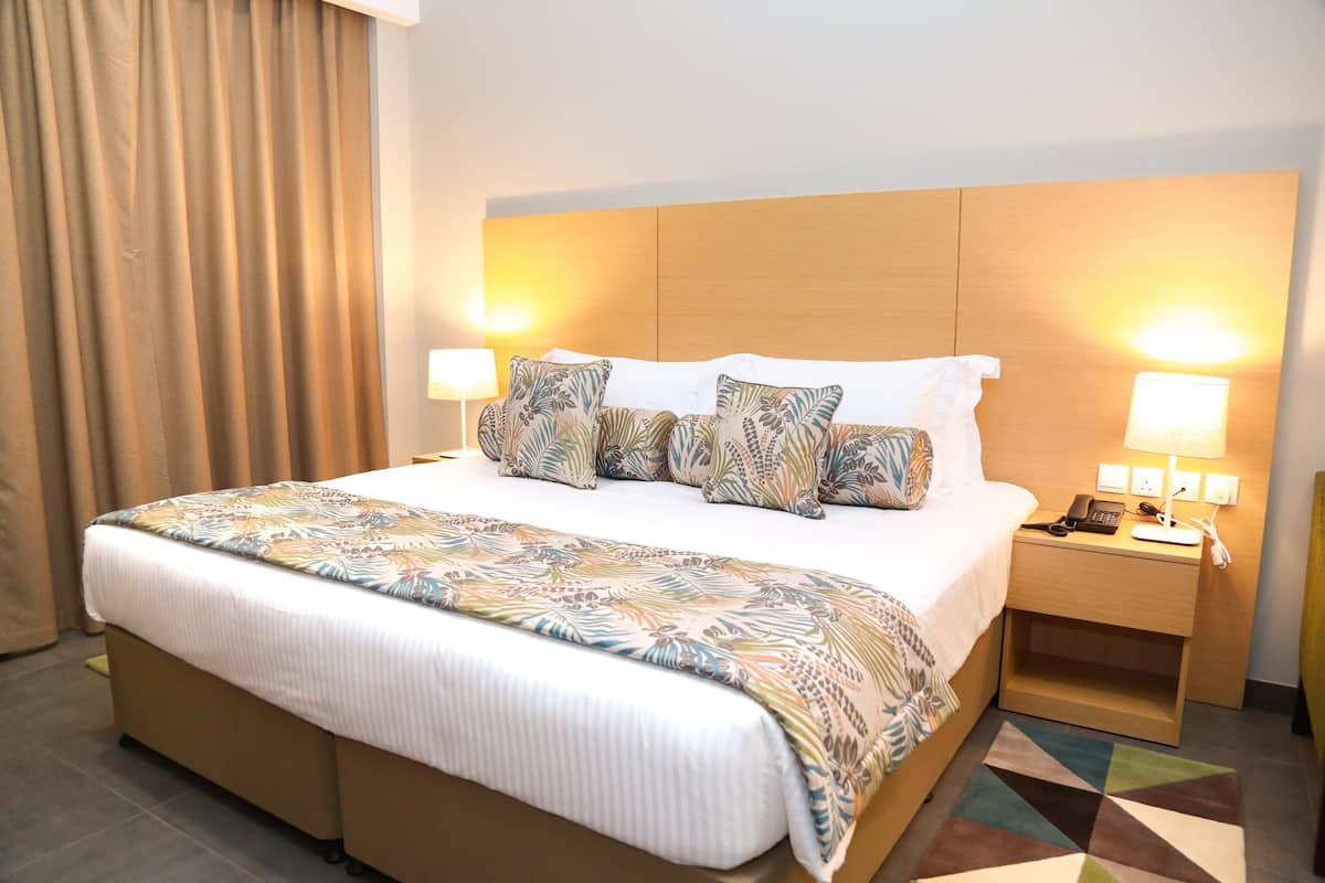 Una habitación de hotel con una cama grande, dos lámparas de noche, una mesita de noche y una alfombra estampada.
