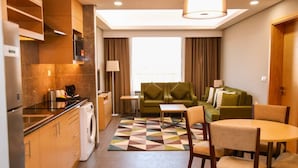 A compact hotel room with a kitchenette, a sofa, a dining table, and a patterned rug. - Ayla Ibri Hotel and Mall (Ibri)