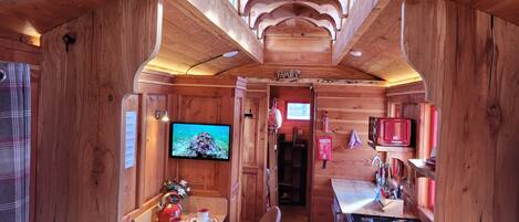 A wooden cabin interior with a dining area, kitchen, and a television.