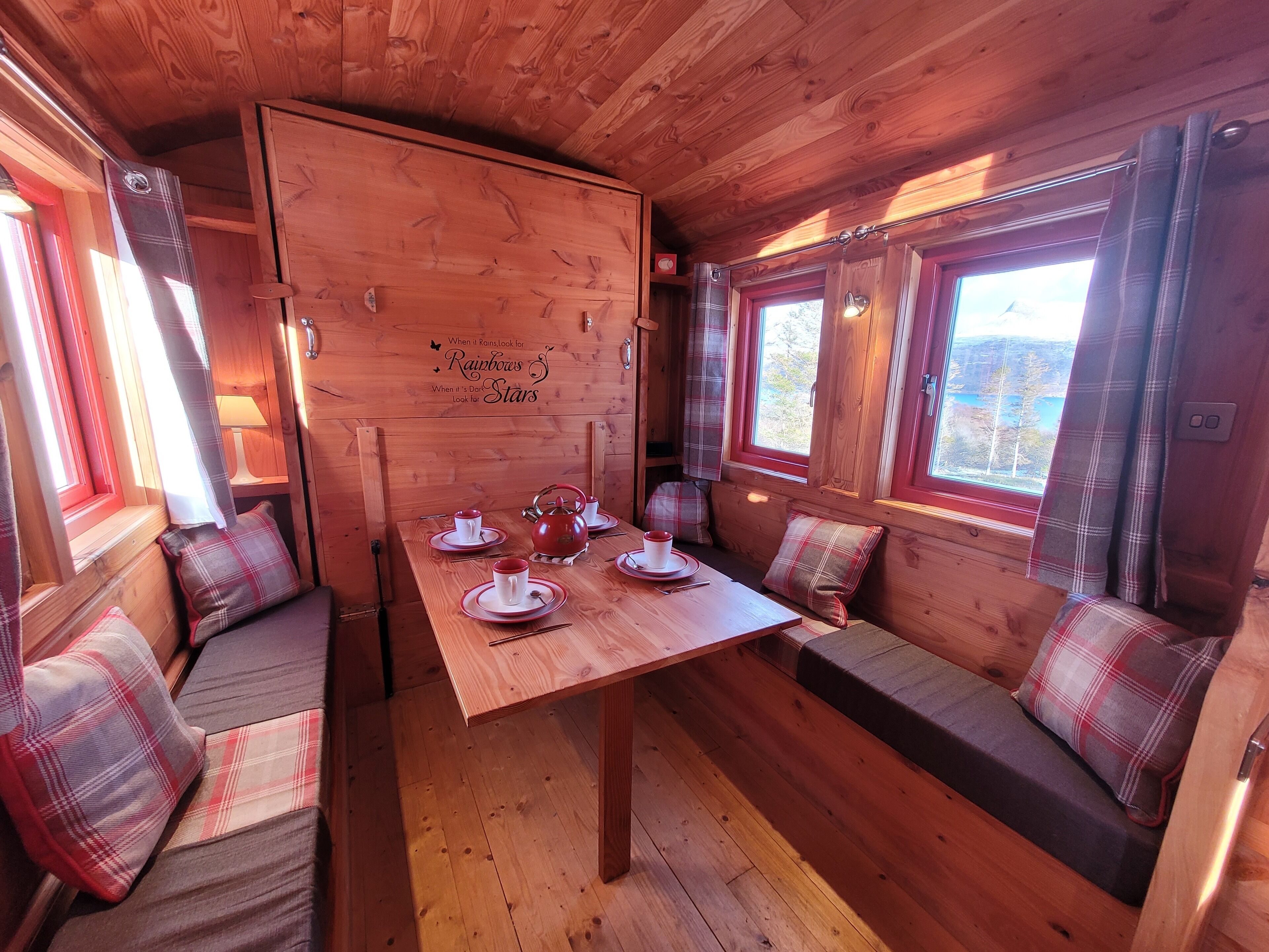 Interior acogedor de una cabaña con una mesa de madera preparada para tomar té, cojines de cuadros y un banco.